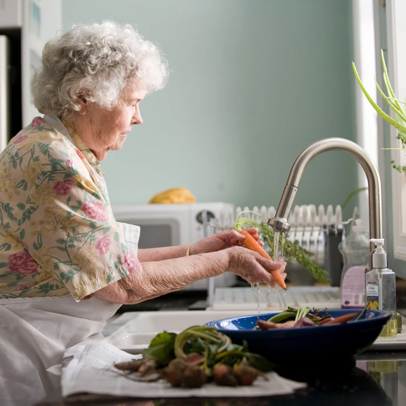 An elderly woman washing carrots in a sink