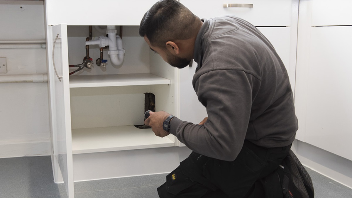 A maintenance worker carrying out a repair beneath a kitchen sink.