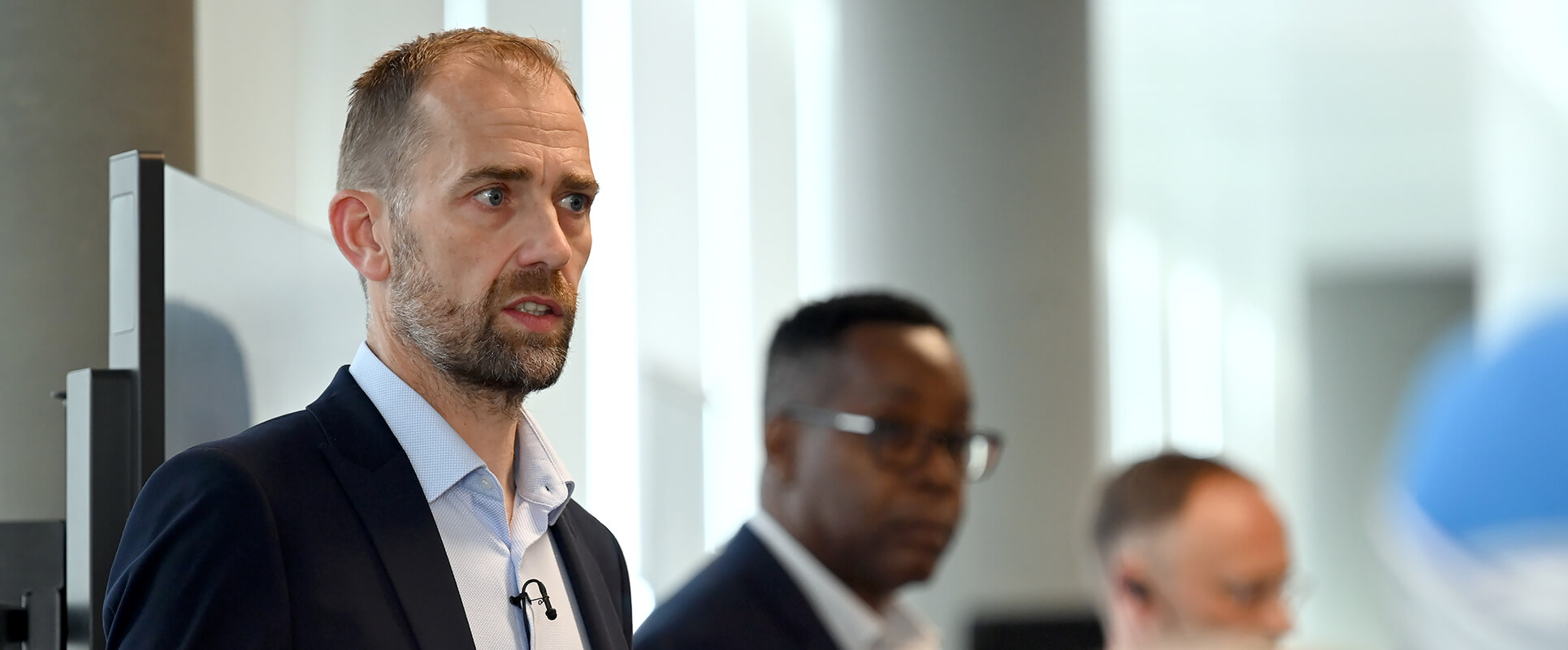 L&Q Leadership team member speaking at an event, with colleagues in the background, in a modern office setting