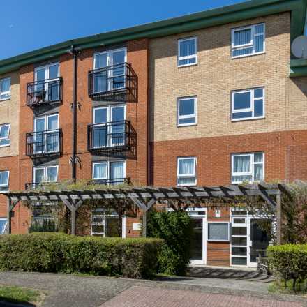 Exterior view of a multi-storey residential building with balconies, landscaped hedges, and a covered entrance.