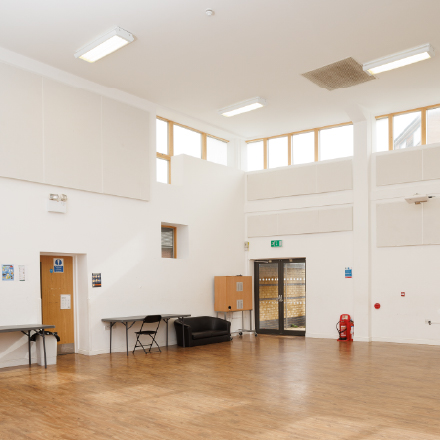 Large multi-purpose community hall with high ceilings, wooden flooring, and flexible space for events, meetings, and activities.