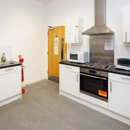 Modern communal kitchen with cooking facilities, worktops, storage cupboards, and appliances.
