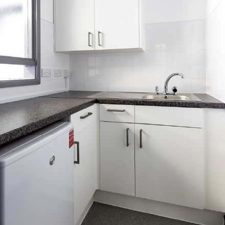 Compact kitchenette with cupboards, sink, worktop, and under-counter fridge.
