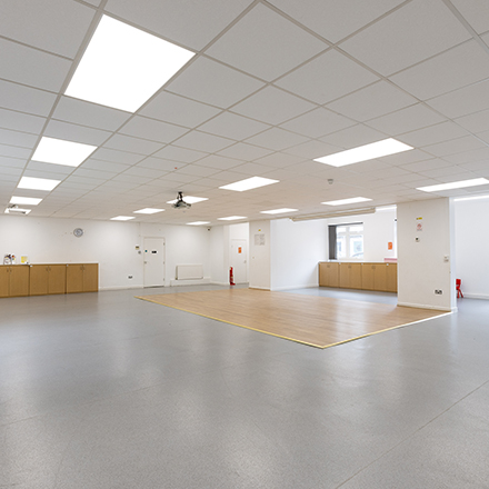 Large open hall with overhead lighting, storage units, and a designated floor area for events and activities.