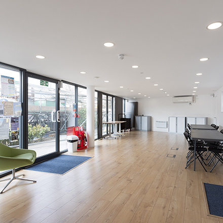 Bright open-plan community room with floor-to-ceiling windows, seating, and flexible space for activities and events.