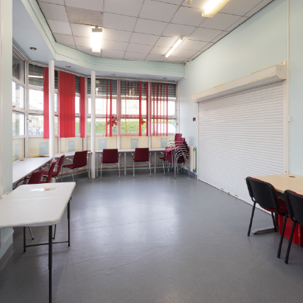 Flexible room with tables, chairs, and natural light, designed for meetings, workshops, training sessions, and community gatherings.