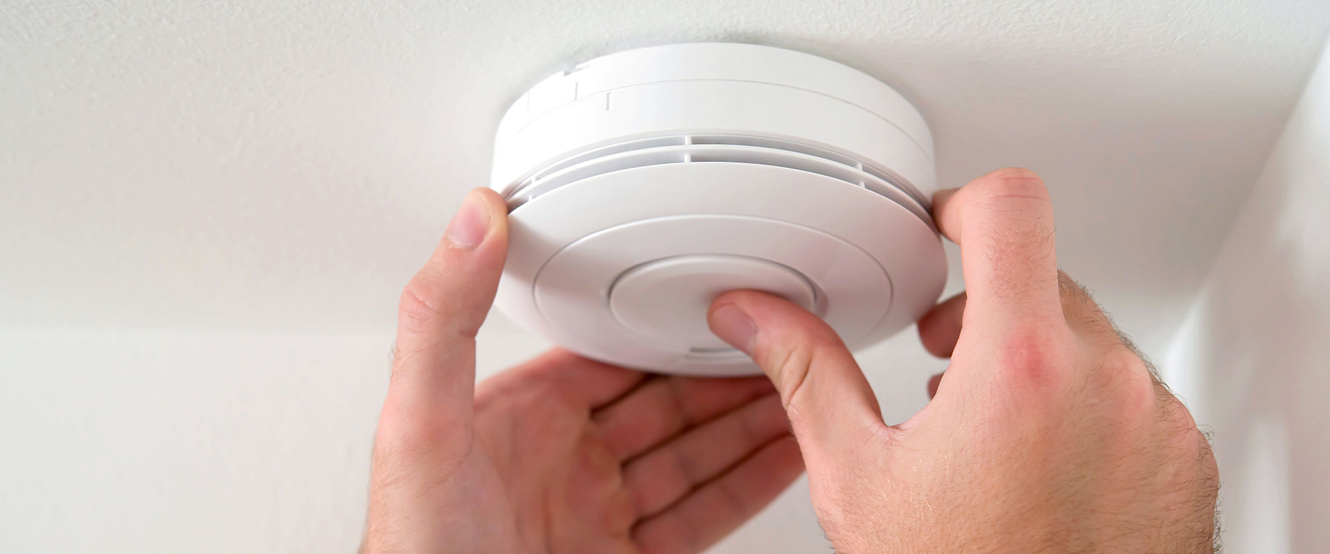 A person's hands adjusting a smoke alarm