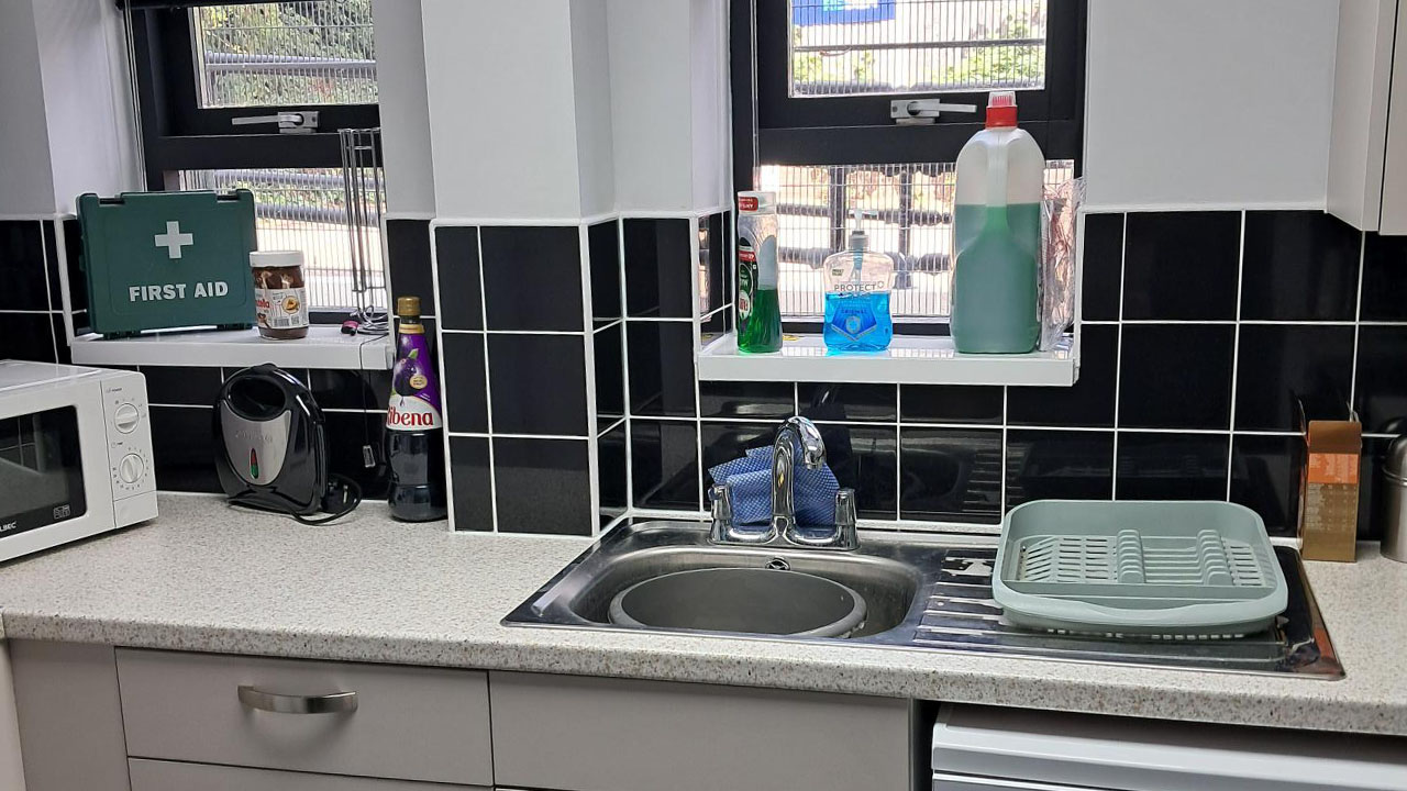 Model Kitchen in Major Works hub showing off new splash back black tiling, worktops, sink and cabinets. Decorated with kitchen items.