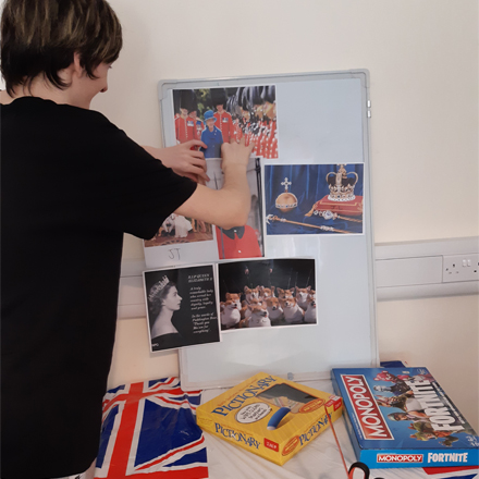 A boy sticking pictures of Queen Elizabeth II on a board