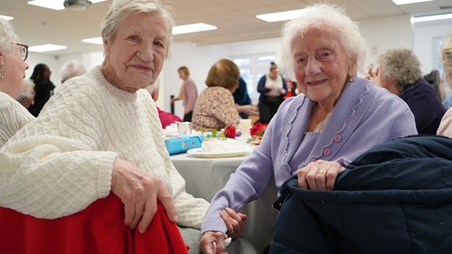 Two elderly ladies sat next to one another smiling at the camera