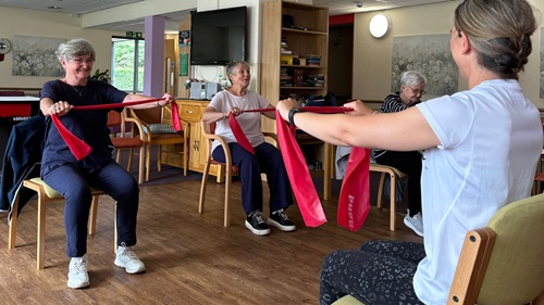 Coach guiding seated resistance band workout for seniors in a community center.