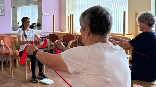 Seated resistance band workout for seniors in a community center following a coach's guide.