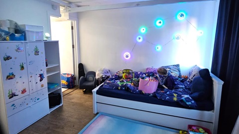 Child sitting on a bed playing with toys and sensory items in a softly lit sensory bedroom.
