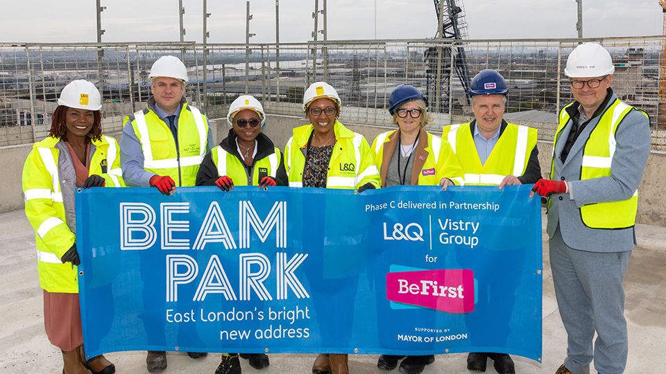 Project partners from L&Q, Vistry Group and Be First celebrate Beam Park topping out milestone, holding a blue banner on site.
