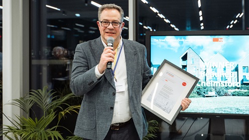 A man holding a microphone and displaying an award certificate, sharing insights or acceptance remarks.