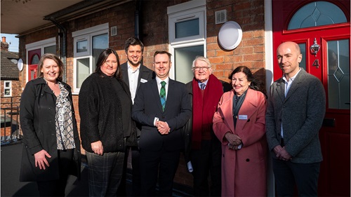 Group photo outside red door – Seven L&Q and Trafford council staff stand together smiling outside a red door, with a brick building in the background.