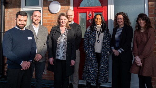 Seven L&Q staff standing in front of the same red door, smiling.