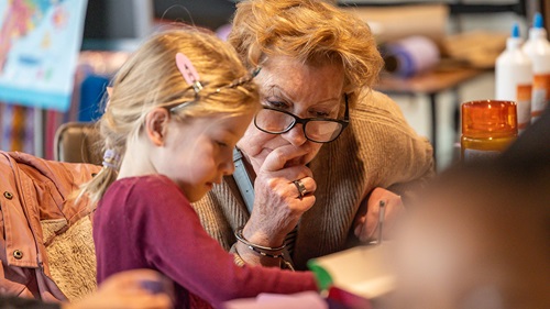 Young person with purple top sat drawing alongside an adult in a beige cardigan, both focused at on the task.