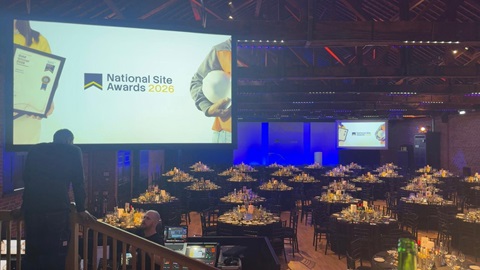 Large indoor venue set up for an awards ceremony, with round dining tables, stage lighting, and screens displaying “National Site Awards 2026.”