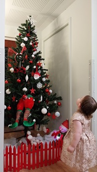 Young child looking up at a Christmas tree decorated with red and white baubles and an elf
