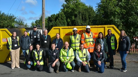 A group of people stood in front of a yellow skip
