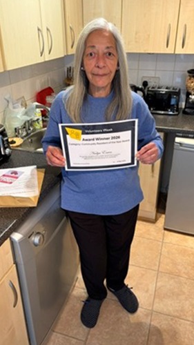 Nadya Enver standing in a kitchen holding an award certificate, with cupboards and appliances in the background.