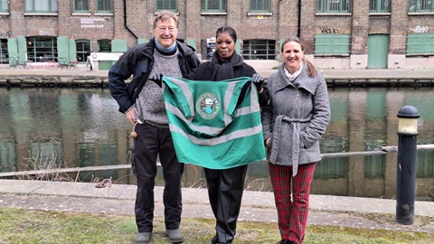 Three people holding Lower Regents Coalition flag by canal