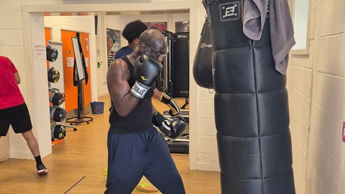 An older man wearing boxing gloves practicing punches on a standing punching bag inside a gym.