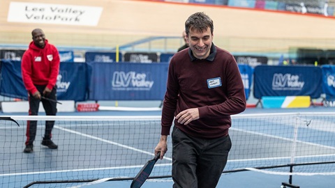 Man smiling while playing pickleball on an indoor court at Lee Valley VeloPark