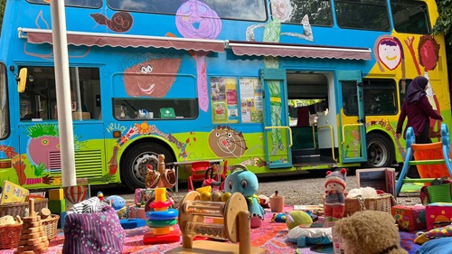Picnic blanket and toys on a blanket outside of a colourful bus