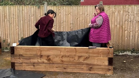 Volunteers lining wooden planter with black sheeting for planting