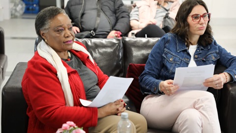 Two women seated, reading papers during community event