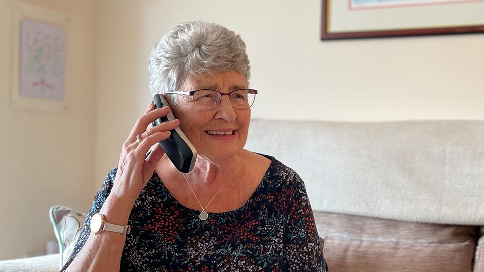 Elderly woman sat on sofa, holding a smart phone to her ear