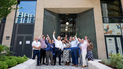 Colleagues gathered for joyful ribbon cutting ceremony outside Key Bridge homes. All cheering to the camera.