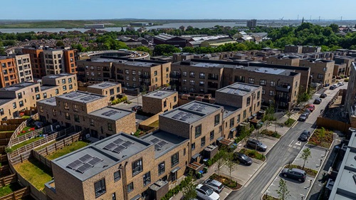 erial view of a modern residential development with brick apartment blocks, houses, solar panels, and surrounding greenery.