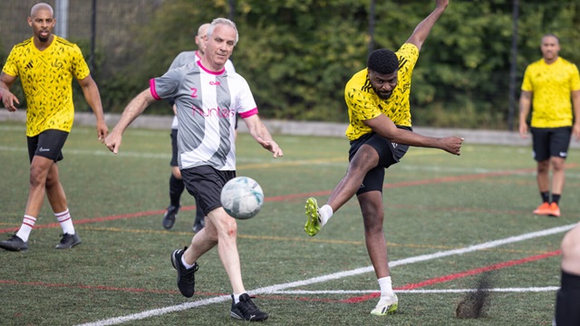 Football player in yellow kit takes a powerful shot while opponent attempts to block