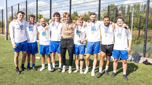 Smiling football team in white and blue kit pose together with medals and a trophy.