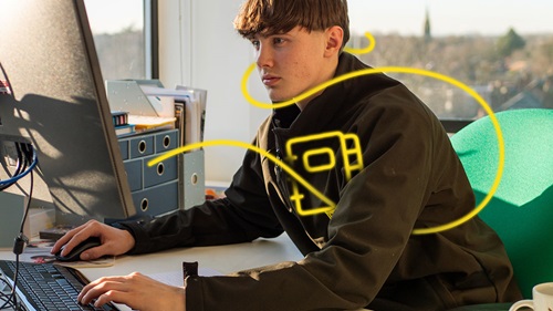George at his desk, working on a computer. Yellow digital lines highlight a book, symbolizing his learning trade skills.