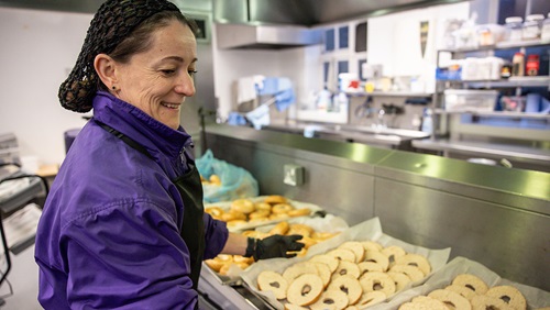Person arranging freshly baked bagels on trays in a kitchen.