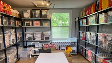 Shelving stocked with donated baby clothes, nappies, toiletries, and essential items organised for distribution to families in need.