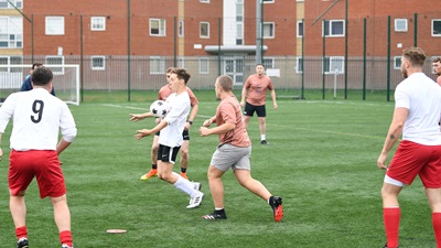 Two football teams playing a match on a grass pitch. One team is wearing salmon pink jerseys and the other have white jerseys.