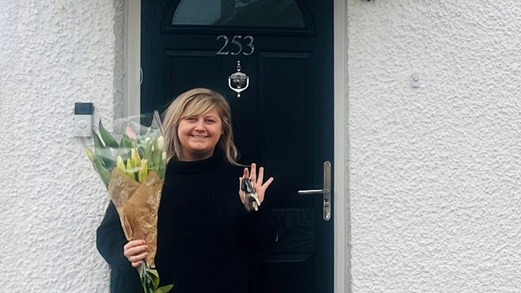 Ms.May stood at the door of her home holding a bouquet of flowers and keys