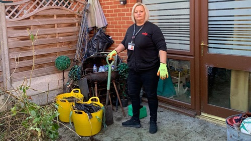 Worker standing with gardening tools next to cleared garden waste