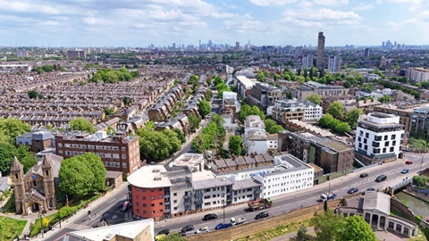 Aerial view of a London neighbourhood with rows of terraced houses, tree-lined streets, and the city skyline in the distance.