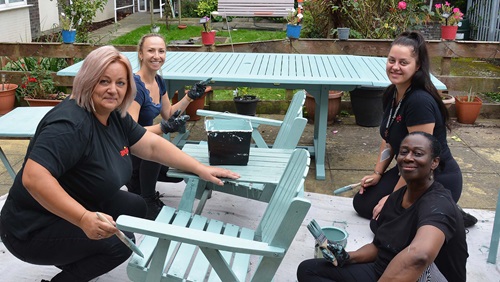 Four Axis volunteers painting garden furniture with teal blue.