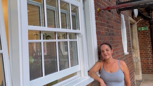 Sally stood outside her property near the windows. She is stood to the right of the image leaning her arm on the sill.