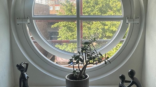 View of circular windows from inside Sally's house. On the inside sill are two abstract black sculpture's sitting each side of a plant pot