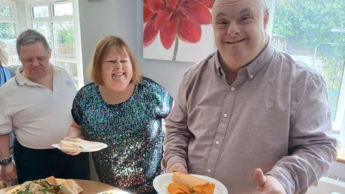 People serving themselves food from a buffet table at a care home gathering.