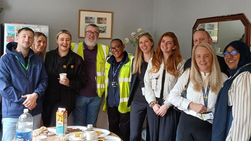 Group gathered around a refreshment table during a community care home visit.
