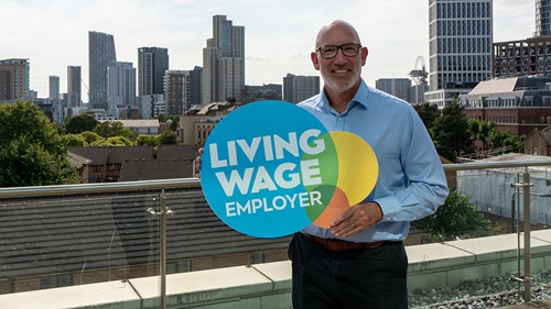  Tom Nicholls, Executive Group Director of Human Resource holding a sign with Living Wage Employer logo on
